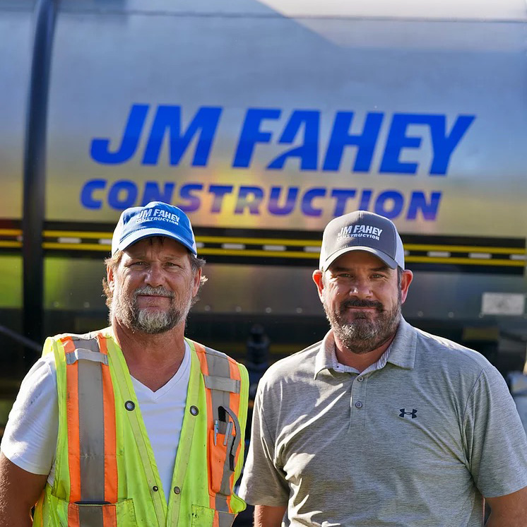jm fahey construction company logo behind two men