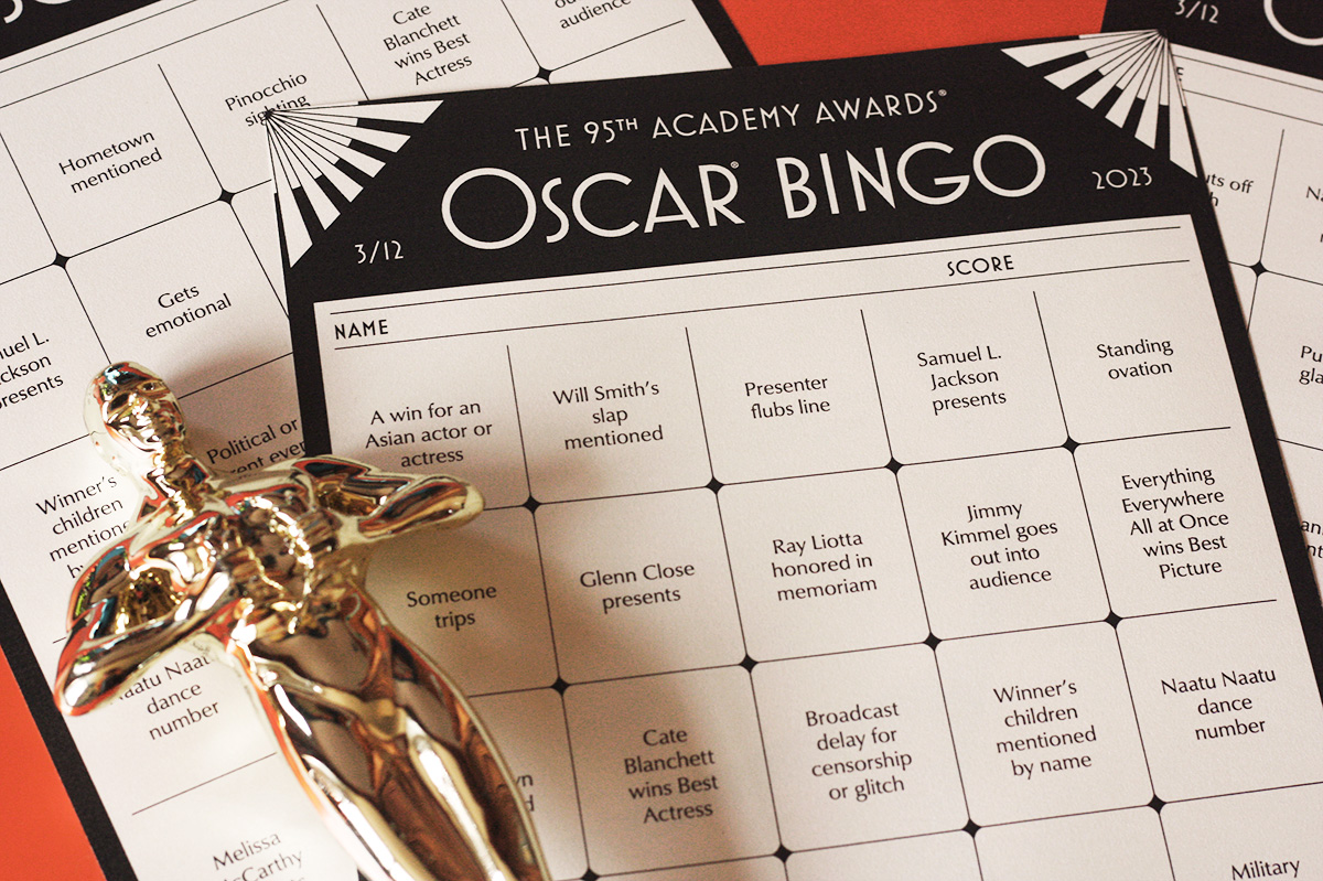 2023 oscar bingo card in an art deco style on table with gold Oscar statue