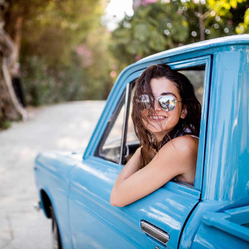 Young woman with sunglasses leaning out the window of a turquoise pickup truck