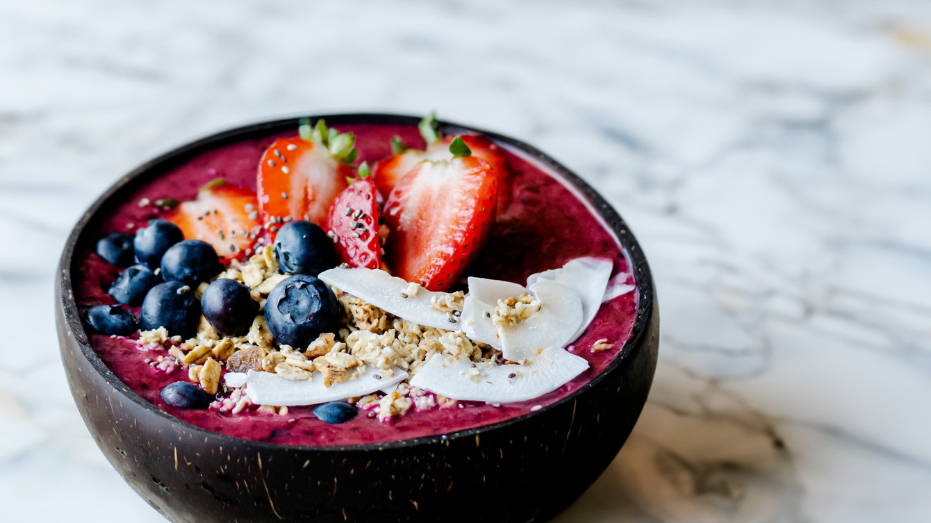Bowl filled with acai, strawberries, blueberries, granola and coconut sitting on a marble countertop